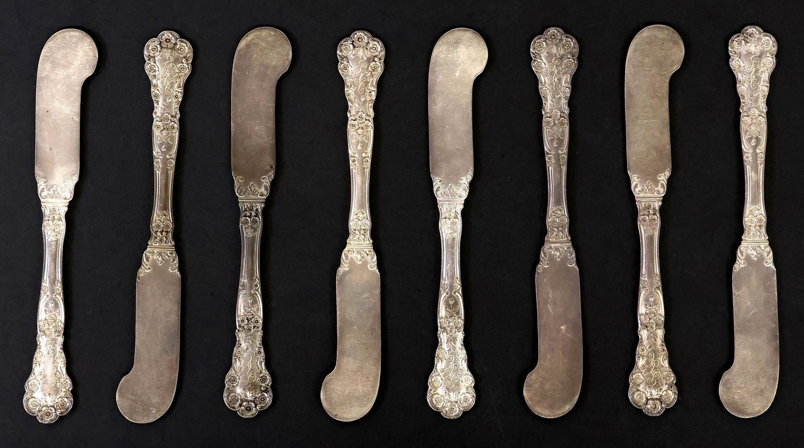 (8) AMERICAN J.E. CALDWELL & CO. STERLING SILVER FLAT BUTTER SPREADERS: (lot of 8) American sterling silver flat handle butter knives, J.E. Caldwell and Company, with flowers and scrolling foliate motifs, triple monogram SAA, the group overall with surface wear, approx 6"