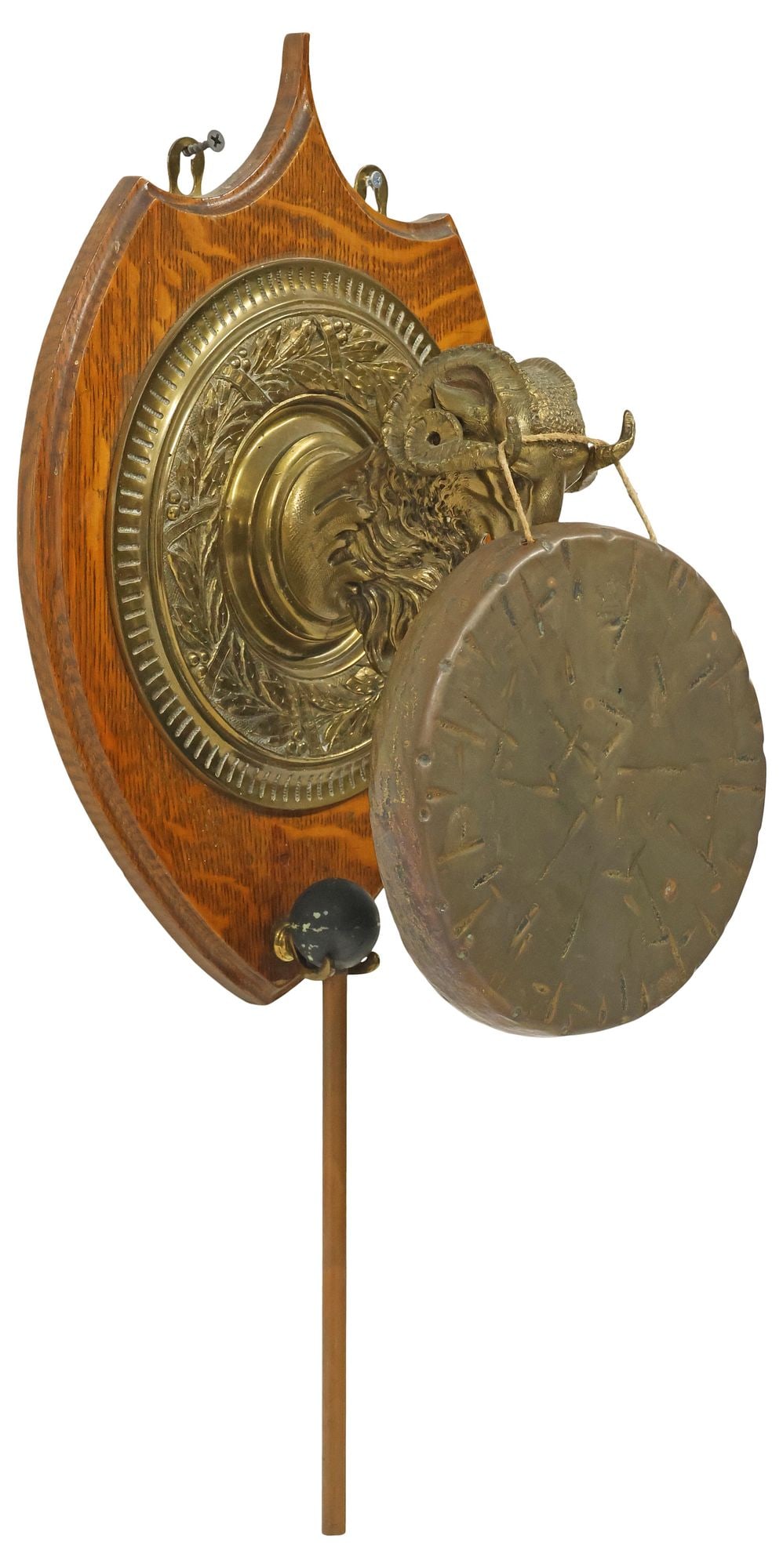 ENGLISH EDWARDIAN OAK & BRASS RAMS HEAD DINNER GONG: English Edwardian oak and brass dinner gong, early 20th c., having a gilt metal ram's head in a surround of laurel and berries, shield form oak mount, suspending a textured disc marked Burmese,