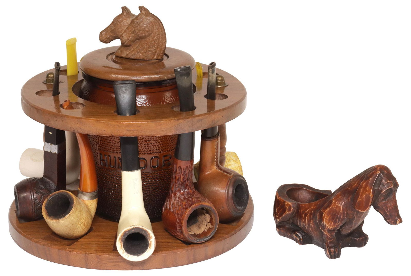 (LOT) VINTAGE WOOD PIPE CADDY WITH HUMIDOR, TOBACCO PIPES & DOG-FORM STAND: (lot) Vintage tiered wood pipe caddy and accessories, circular frame with nine pipe slots, centering Dun-Rite Wood Nov Incorporated molded amber glass humidor, marked Bklyn. N.Y. underfoot, the cover 