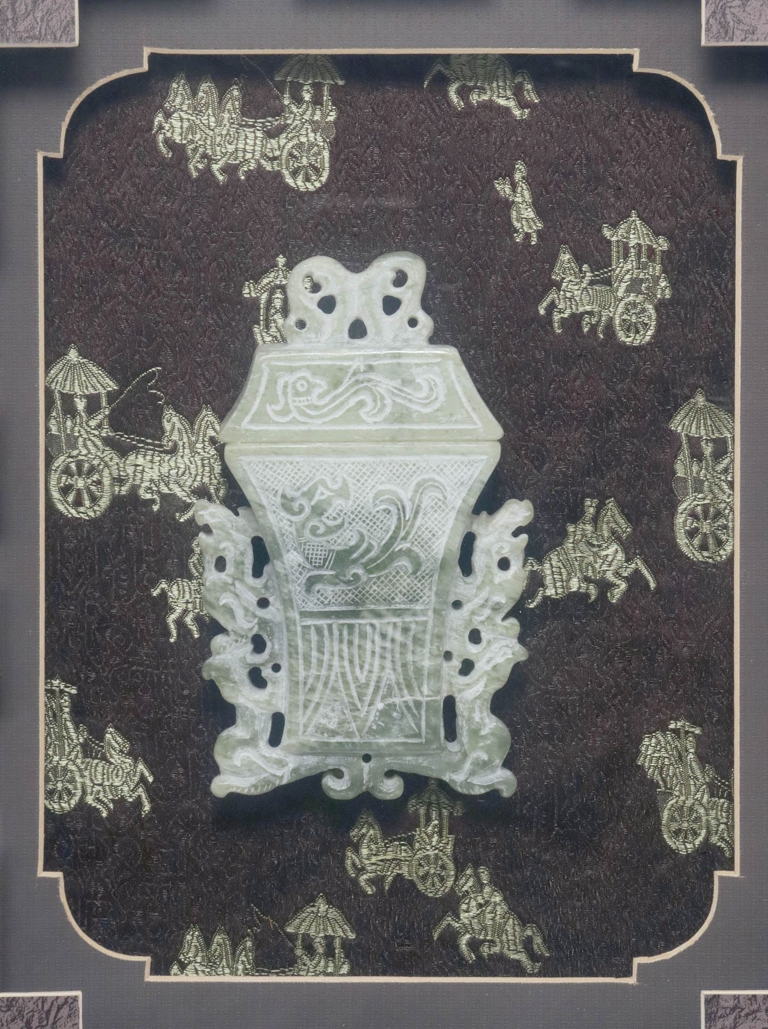 CHINESE CARVED GREEN HARDSTONE COVERED VASE IN SHADOWBOX FRAME: Chinese carved green hardstone vase and cover, waisted lid and tapered body with incised figural decoration, flanked by pierced scrolled dragon handles, housed in faux bamboo shadowbox frame, mounted 