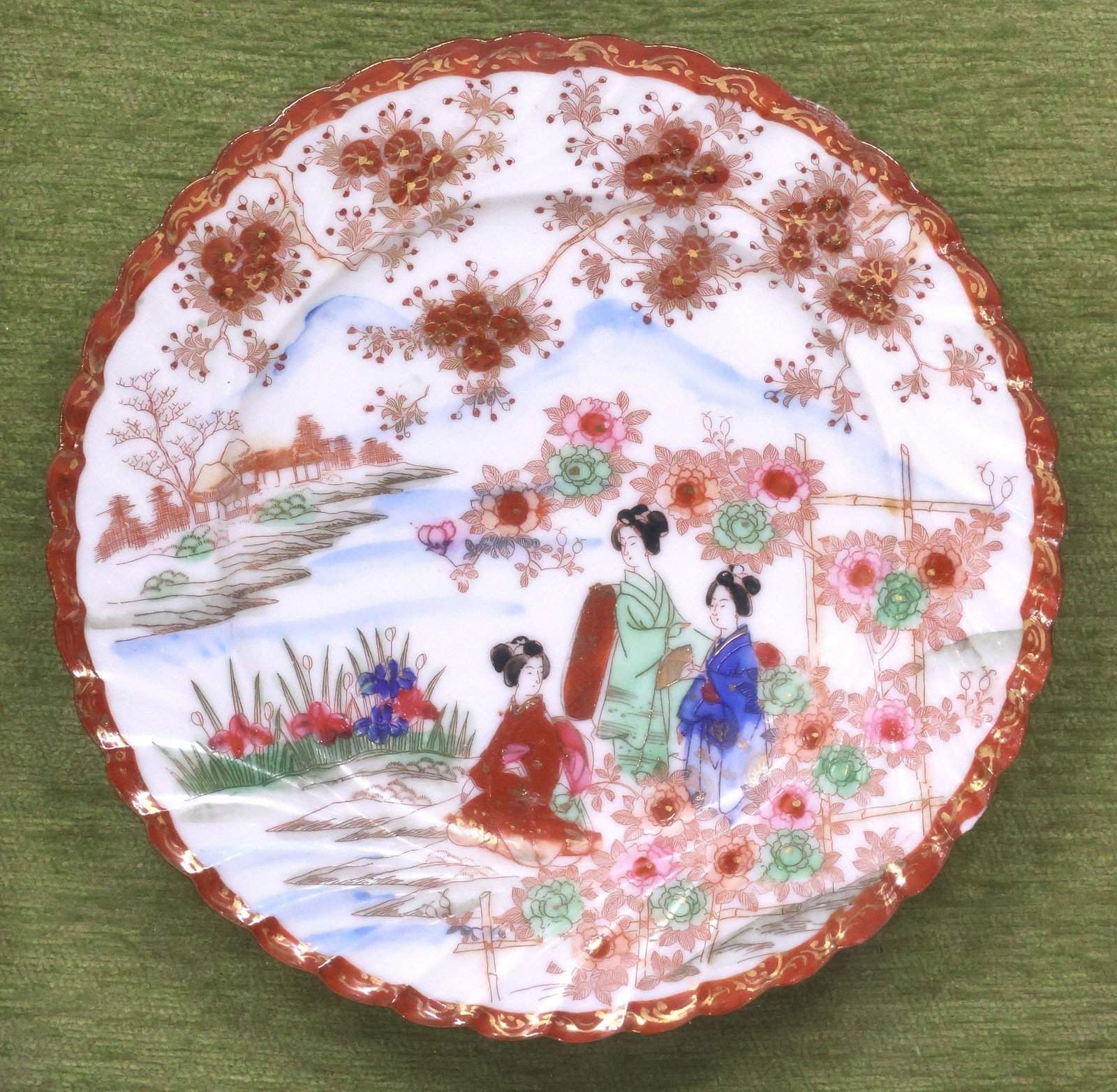 JAPANESE AKA-E KUTANI PORCELAIN PLATE IN GILTWOOD SHADOWBOX FRAME: Framed Japanese aka-e kutani porcelain plate, with parcel-gilt enameled scene of three robed geishas in a courtyard garden, fluted border and scalloped rim, housed in a giltwood shadowbox frame with p