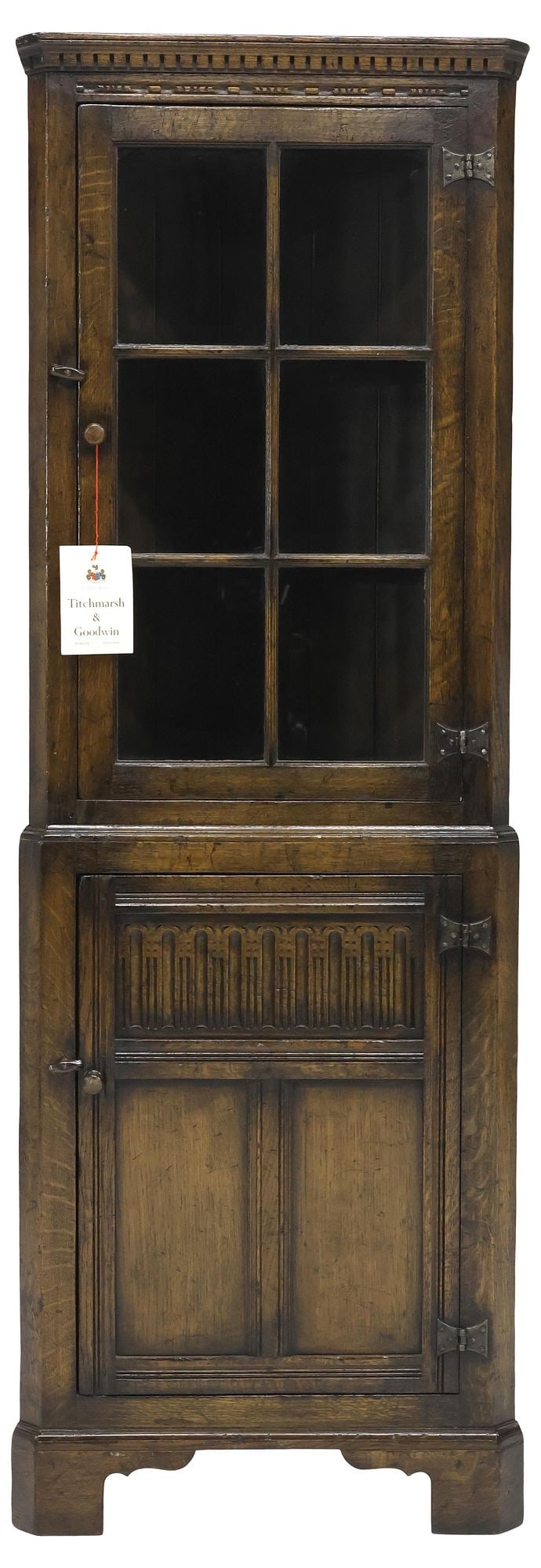 ENGLISH TITCHMARSH & GOODWIN CARVED OAK CORNER CABINET: English oak corner cabinet, Titchmarsh & Goodwin, Suffolk, 20th c., having dentil-molded cornice, above cabinet door with mullioned panes of glass, lower case with carved paneling and single door,