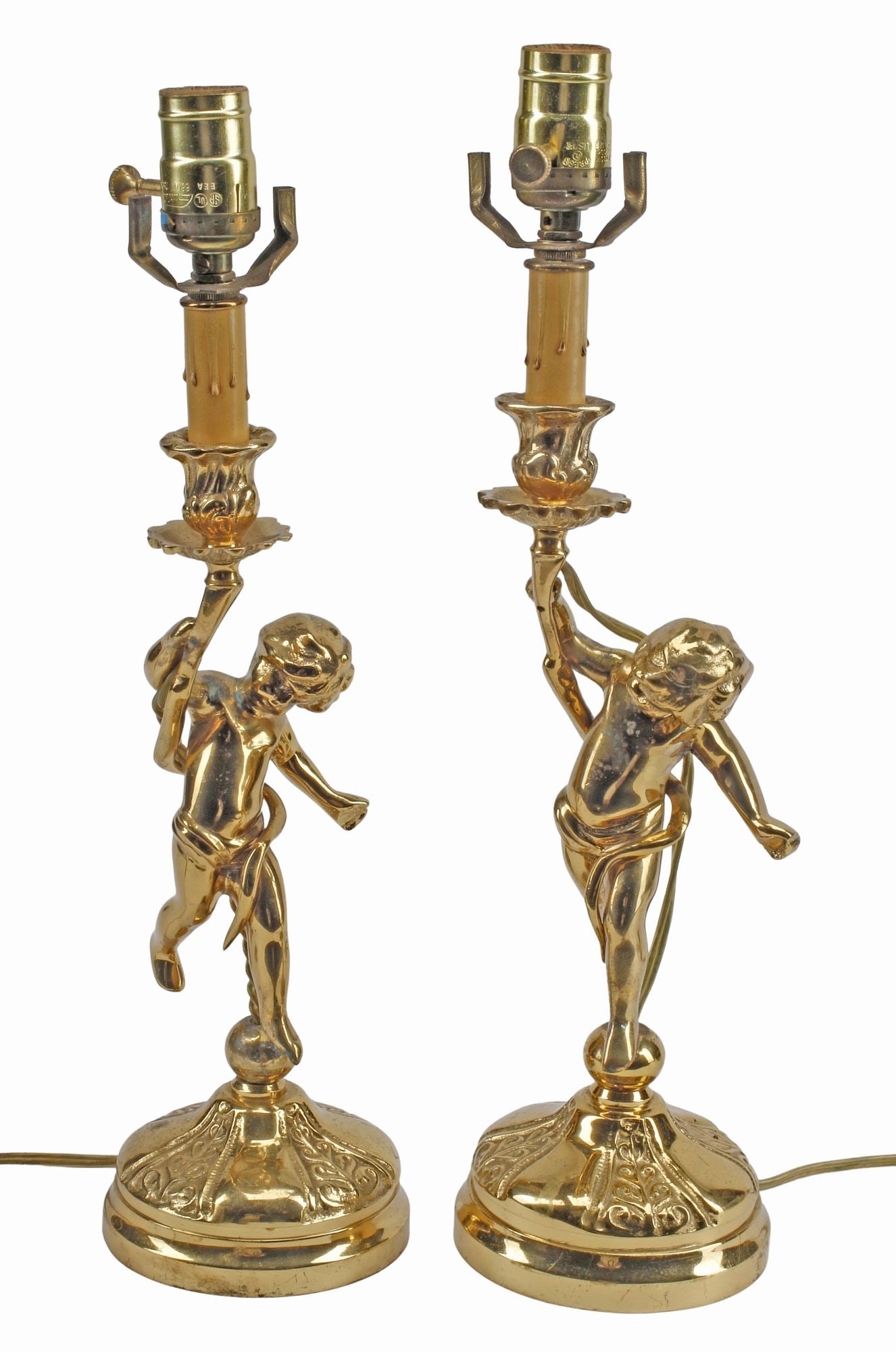(2) CONTINENTAL FIGURAL BRASS PUTTI CANDLESTICK TABLE LAMPS: (pair) Continental gilt-metal figural table lamps, 20th c., likely converted from candlesticks, each modeled as a putto supporting a foliate candle cup, on a cast circular base with scroll decoration,