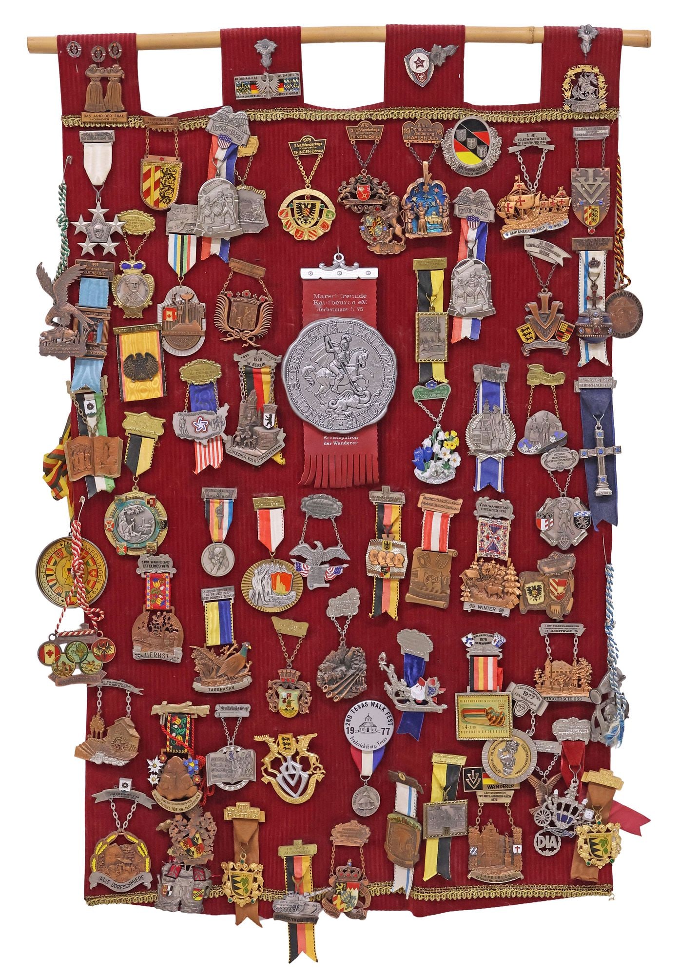 HANGING COLLECTION OF COMMEMORATIVE WANDERING CLUB MEDALS, TX & EUROPE: Collection of seventy-four wandering club medals, hung on a red fabric display banner, highlights include: (one) featuring a tank, inscribed "Reservisten des Heeres (Army Reserves)," (one)commemoratin