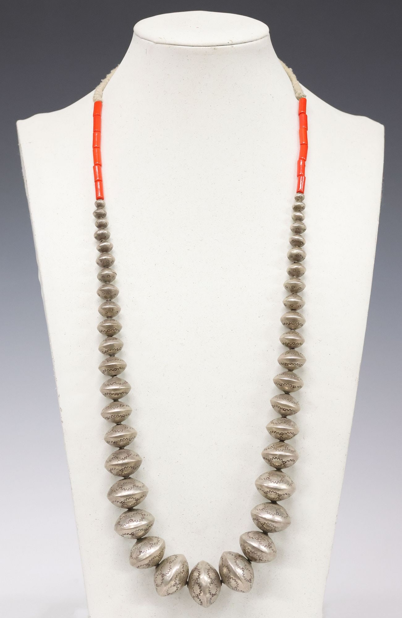 UNUSUAL NAVAJO PEARLS SILVER STAMPWORK BENCH BEAD NECKLACE: Native American silver (content unknown) necklace, likely Navajo/ Dine, forty-one graduated bench beads, all with varied starburst and circular stampwork motifs, cylindrical red coral beads, ending on