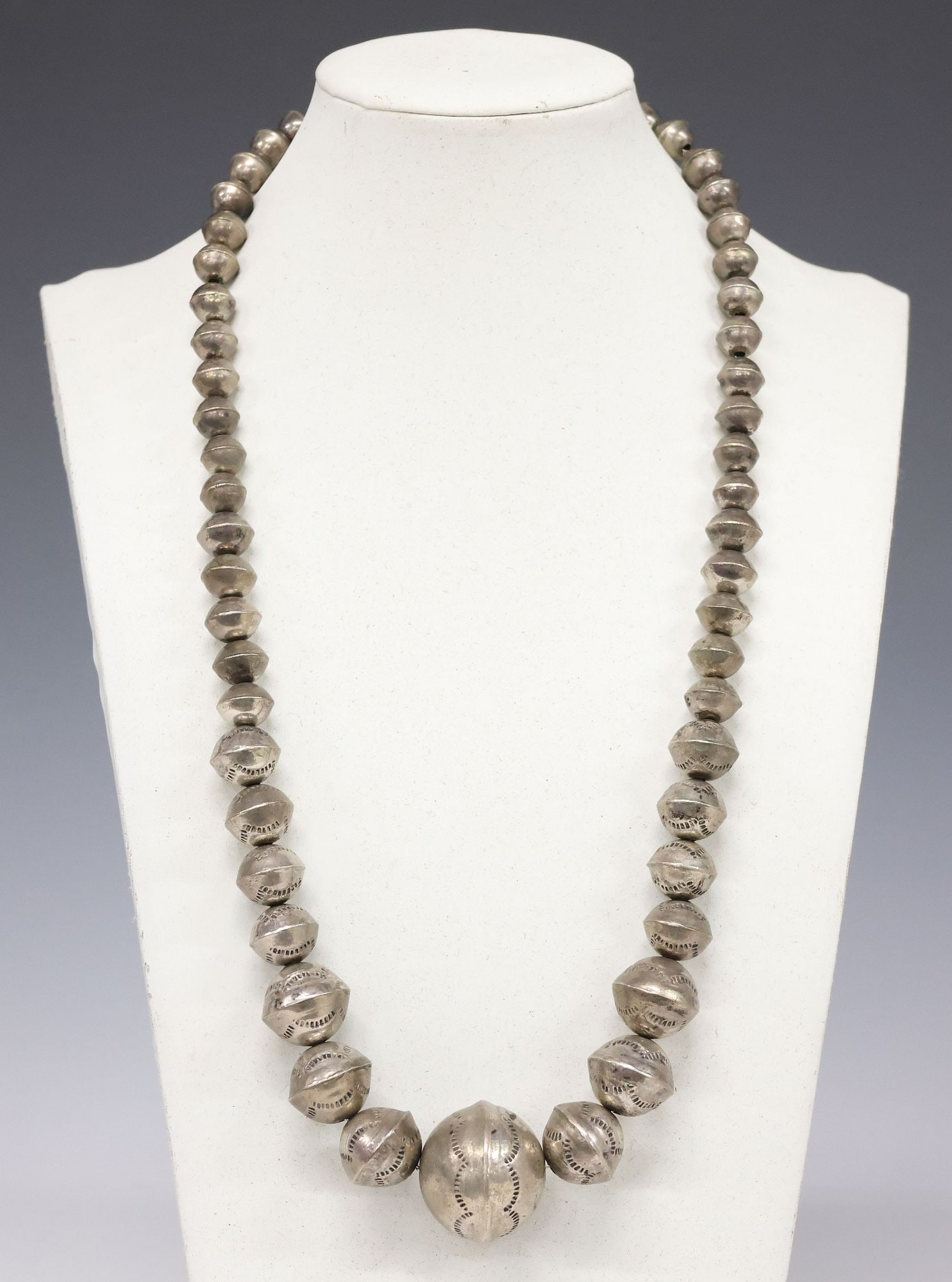 NAVAJO PEARLS SILVER STAMPWORK BENCH BEAD NECKLACE: Native American silver (content unknown) necklace, likely Navajo/ Dine, fifty-one graduated bench beads, (fifteen) with stampwork motifs, conical findings and hook closure, approx 24"l, 64.5 grams (in