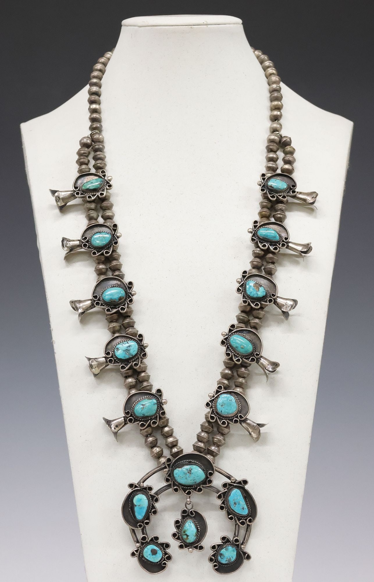 NATIVE AMERICAN SILVER & TURQUOISE CABOCHON SQUASH BLOSSOM NECKLACE: Native American silver (content unknown) and turquoise squash blossom necklace, large split-band naja pendant with shaped plaques, set with freeform turquoise cabochons, framed by (ten) conforming squ
