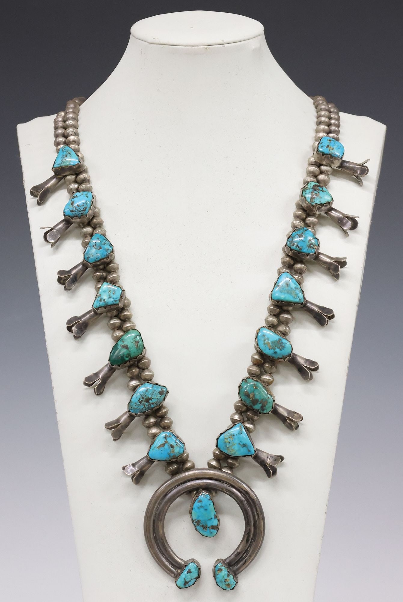 NATIVE AMERICAN SILVER & TURQUOISE CABOCHON SQUASH BLOSSOM NECKLACE: Native American silver (content unknown) and turquoise squash blossom necklace, arched naja pendant with three bezel-set turquoise cabochons, framed by (fourteen) squash blossoms with large freeform t