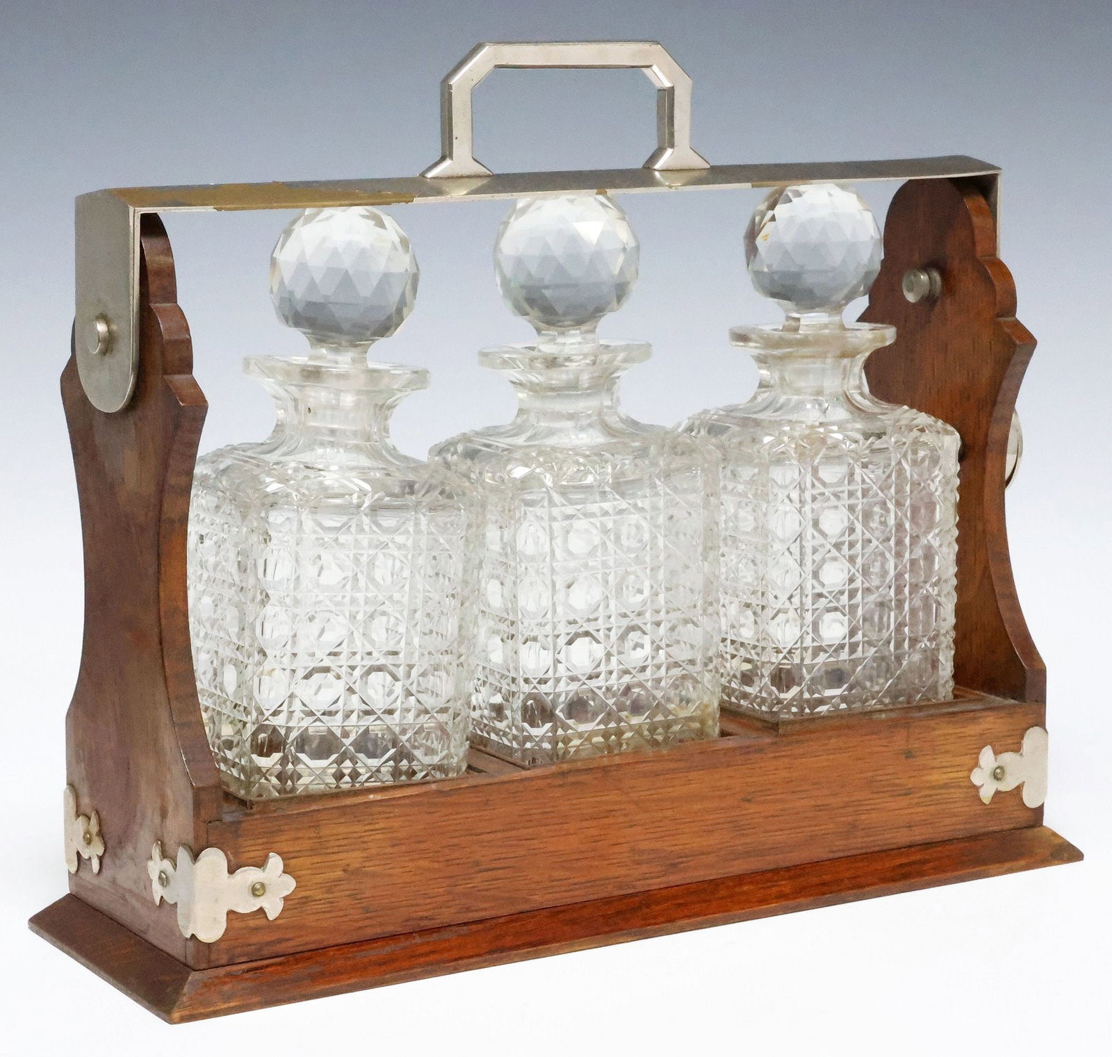 ENGLISH EDWARDIAN OAK & CUT-CRYSTAL LIQUOR CASKET / TANTALUS: English oak tantalus set/ liqueur casket, early 20th c., caddy with silver-plate corner mounts and swing handle with locking mechanism, three squared cut-crystal decanters with faceted spherical stopp