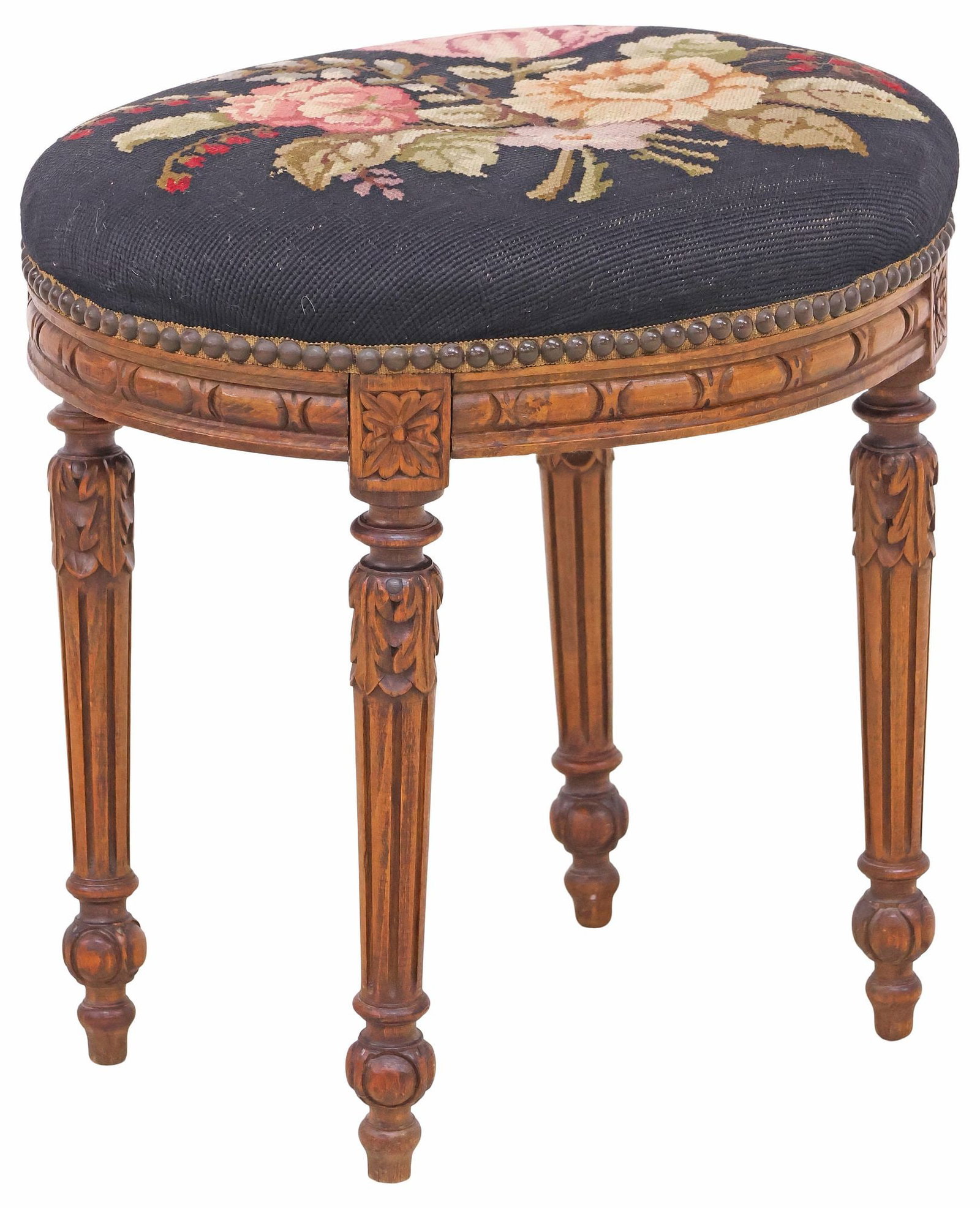 FRENCH LOUIS XVI STYLE NEEDLEWORK-UPHOLSTERED OTTOMAN / FOOTSTOOL: French Louis XVI style carved walnut ottoman/ footstool, late 19th c., padded seat in floral needlework upholstery, with nailhead trim, rising on fluted tapering legs, ending on turned feet, approx 18