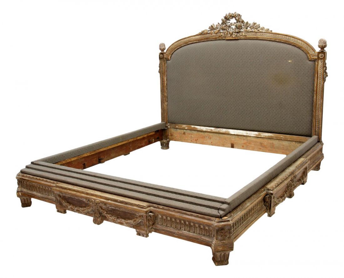LOUIS XVI STYLE FOLIATED & RIBBON CARVED BED: Louis XVI style bed, 19th c., now modified to accommodate a king, the arched headboard crested by a carved ribbon, pineapple finials, the center padded in a continuous white swirl on gray fabric, the