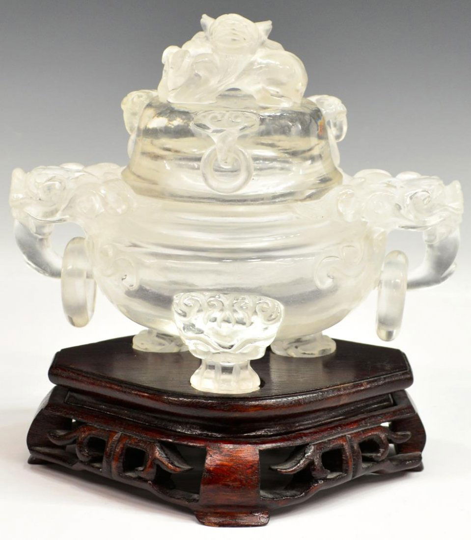 CHINESE CARVED ROCK CRYSTAL INCENSE BURNER: Chinese colorless carved rock crystal incense burner, the lid a dragon head, conforming dragon head ring handles, set on claw feet, pierced wood stand, flakes to rims, crystal: 6"h, 7.5"w, 5"d, overal