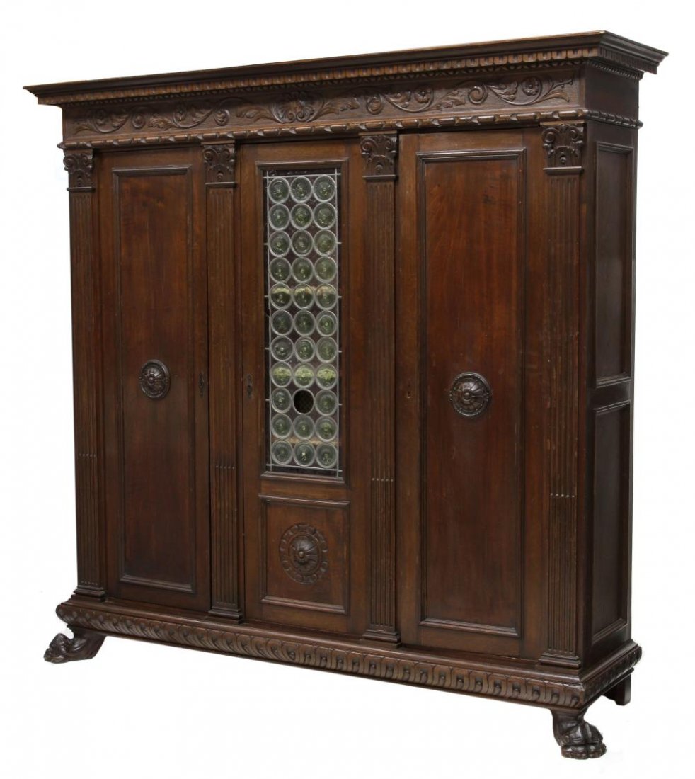 ITALIAN RENAISSANCE REVIVAL TRIPLE BOOKCASE: Italian Renaissance Revival triple bookcase, early 20th c., having a stepped cornice over the carved frieze, a central door with stained glass roundels flanked by two solid doors, rising on large claw