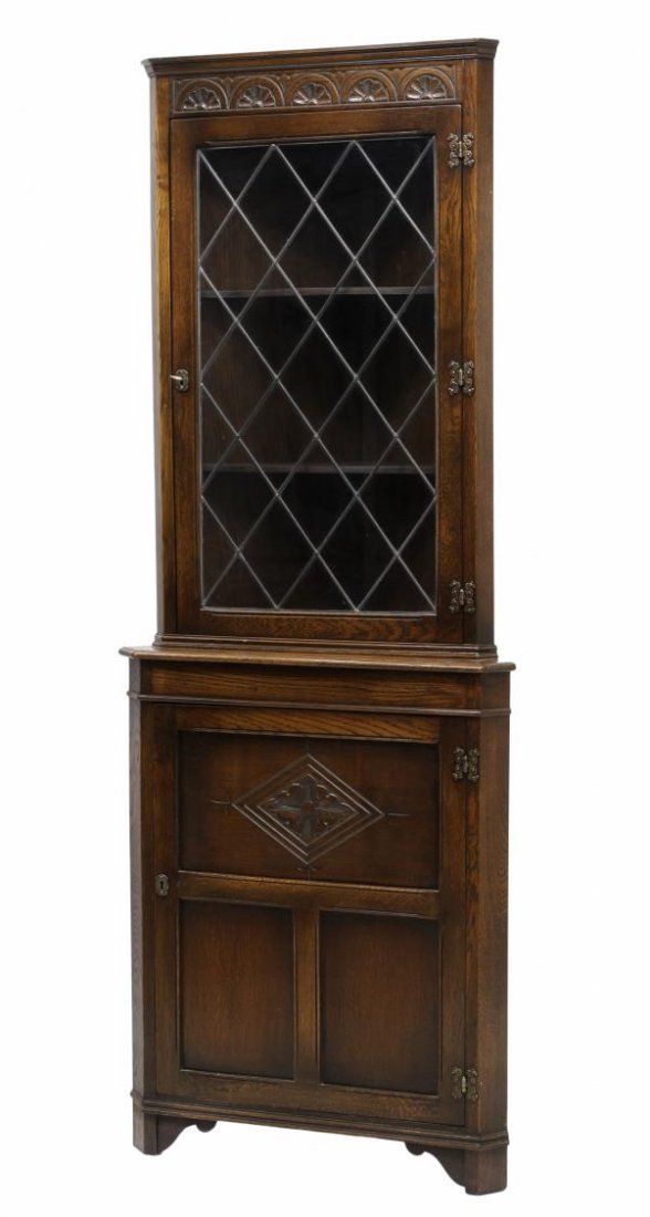 ENGLISH OAK LEADED GLASS CORNER CABINET: English oak corner cabinet, 20th c., a stepped cornice and carved frieze over a single leaded glass door, a lower closed front door opening to shelves, rising on block feet, 72"h, 27"w, 14"d Start Pri