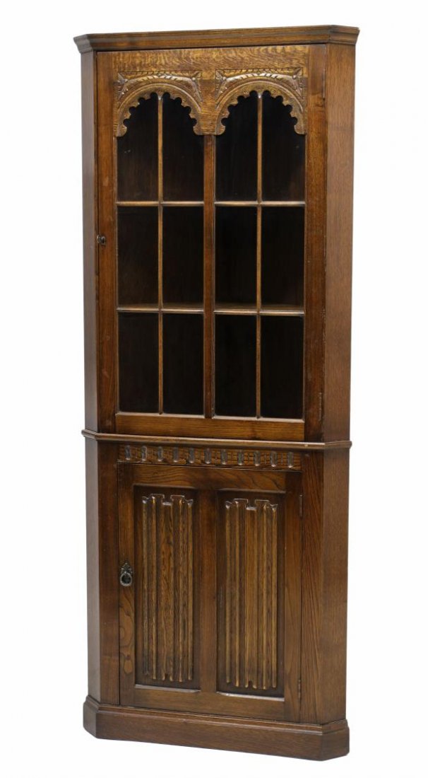 ENGLISH OAK CORNER DISPLAY CABINET: English oak corner cabinet, 20th c., the stepped cornice over a 12 pane glass door with foliate carving, a lower linen fold carved front door, rising on a conforming base, 69"h, 27.75"w, 14.5"d Start 