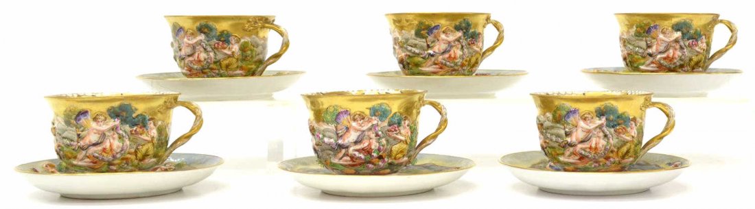 (12) CAPODIMONTE ARMORIAL DECORATED CUPS & SAUCERS: (set) Capodimonte porcelain tableware including (6) cups and (6) saucers, handpainted armorials at the center of each saucer, relief figural decoration overall, heavily gilded accents, crown over N ma