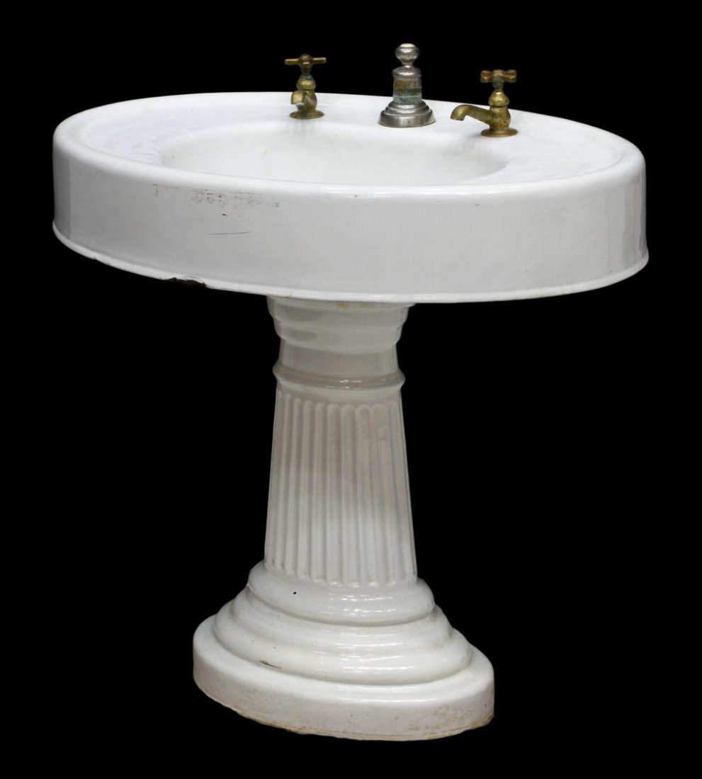 VINTAGE OVAL PORCELAIN PEDESTAL SINK: Vintage oval porcelain iron sink rising on a ribbed pedestal with a stepped oval base, parcel gilt hot and cold faucets, some chippping, loss to porcelain, sink: 31.5"h, 32.75"w, 21.75"d Start Price: 