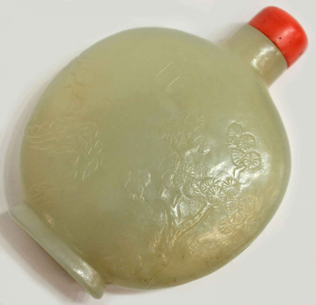 ANTIQUE CHINESE CARVED JADE SNUFF BOTTLE: Chinese jade snuff bottle, 18th c., of pale celadon color, low relief depicting a scene of trees and mountains, body of circular form raised on a splayed foot, orange stopper with intact spoon, 2.5"h