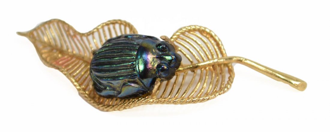 14KT GOLD LEAF BROOCH & IRIDESCENT SCARAB BEETLE: An iridescent art glass scarab beetle, in the manner of Tiffany, mounted on a 14kt gold brooch, in the form of a leaf, chip to end of beetle, 2.25"l; 6.9 grams (inclusive of all materials) *Provenance