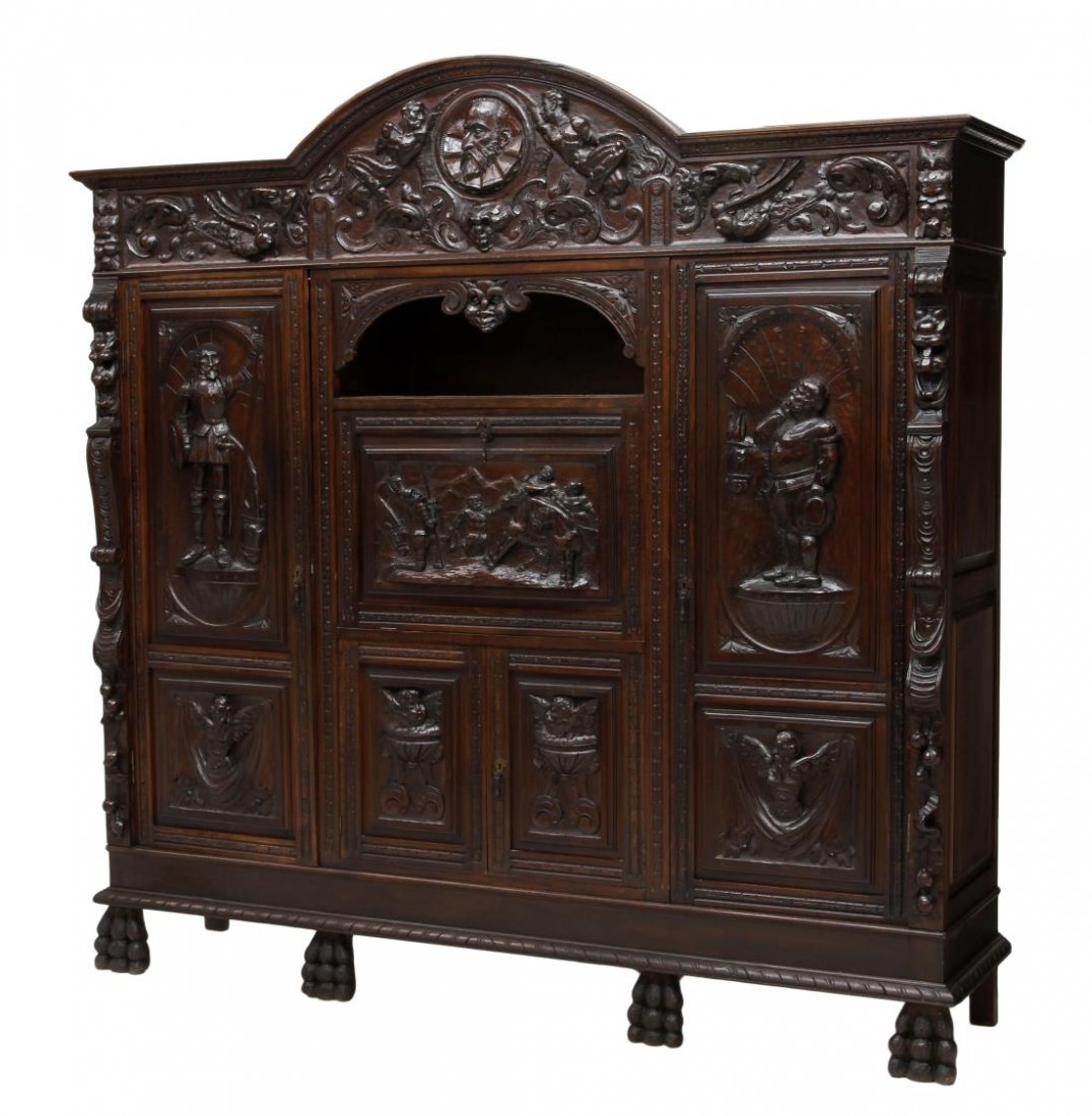 HIGHLY CARVED DON QUIXOTE SPANISH BOOKCASE: Northern Spain walnut secretary bookcase profusely carved in relief, illustrating various scenes from Cervante's Don Quixote, an arched cornice above a figural decorated frieze with additional foliate