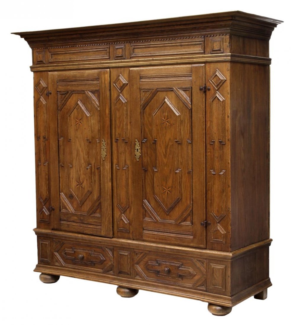 18TH C. GERMAN STAR INLAID OAK SCHRUNK CABINET: German inlaid oak shrunk, 18th c., the projected cornice over a paneled and carved frieze, two doors inlaid with contrasting wood stars hang on short iron hinges, open to a shelved interior, lower dra