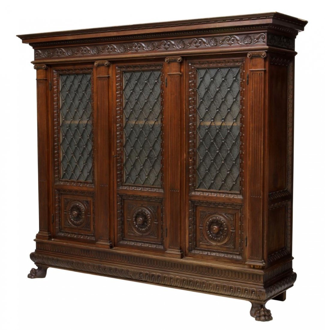 ITALIAN CARVED WALNUT LIBRARY BOOKCASE: Carved mahogany library bookcase, Italy, 19th c., having a stepped cornice over a shell and foliate carved frieze, three pilaster flanked glass front doors faced with open twist metal lattice, interio