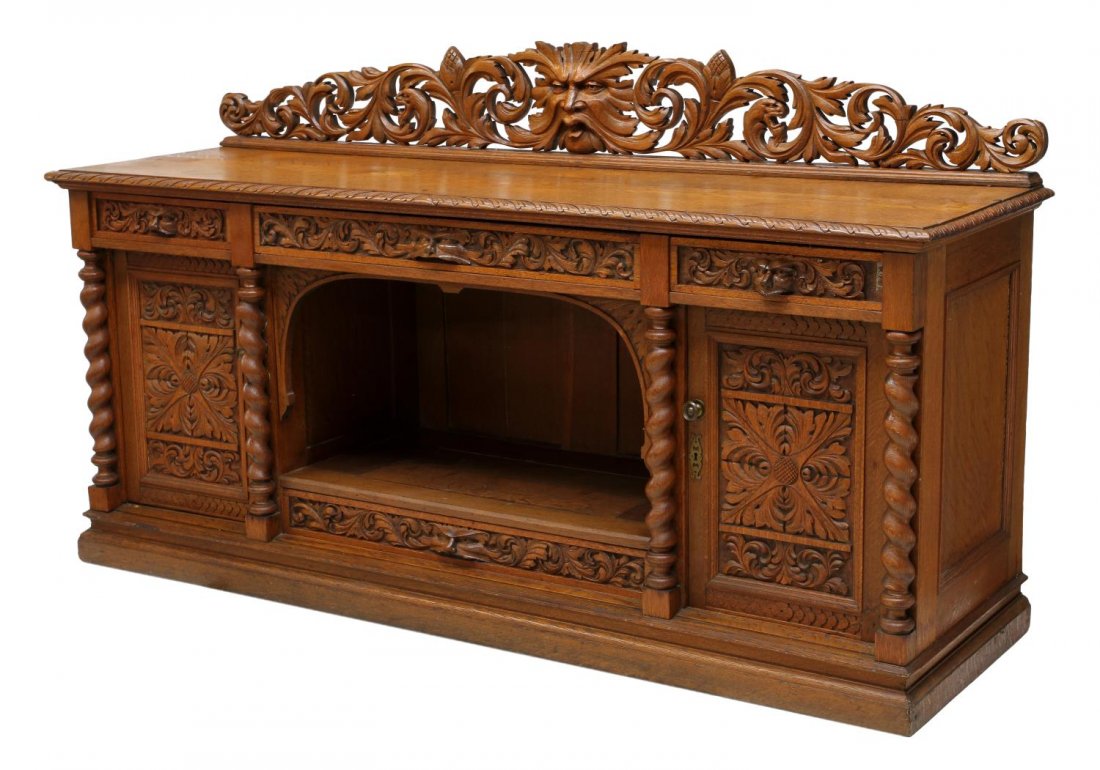 HIGHLY CARVED ENGLISH OAK SIDEBOARD: English oak sideboard accented with carved figural masks, foliate carving and griffins, c. 1900, the pierced carved back over the long rectangular top, three carved frieze drawers, the lower cabinet w