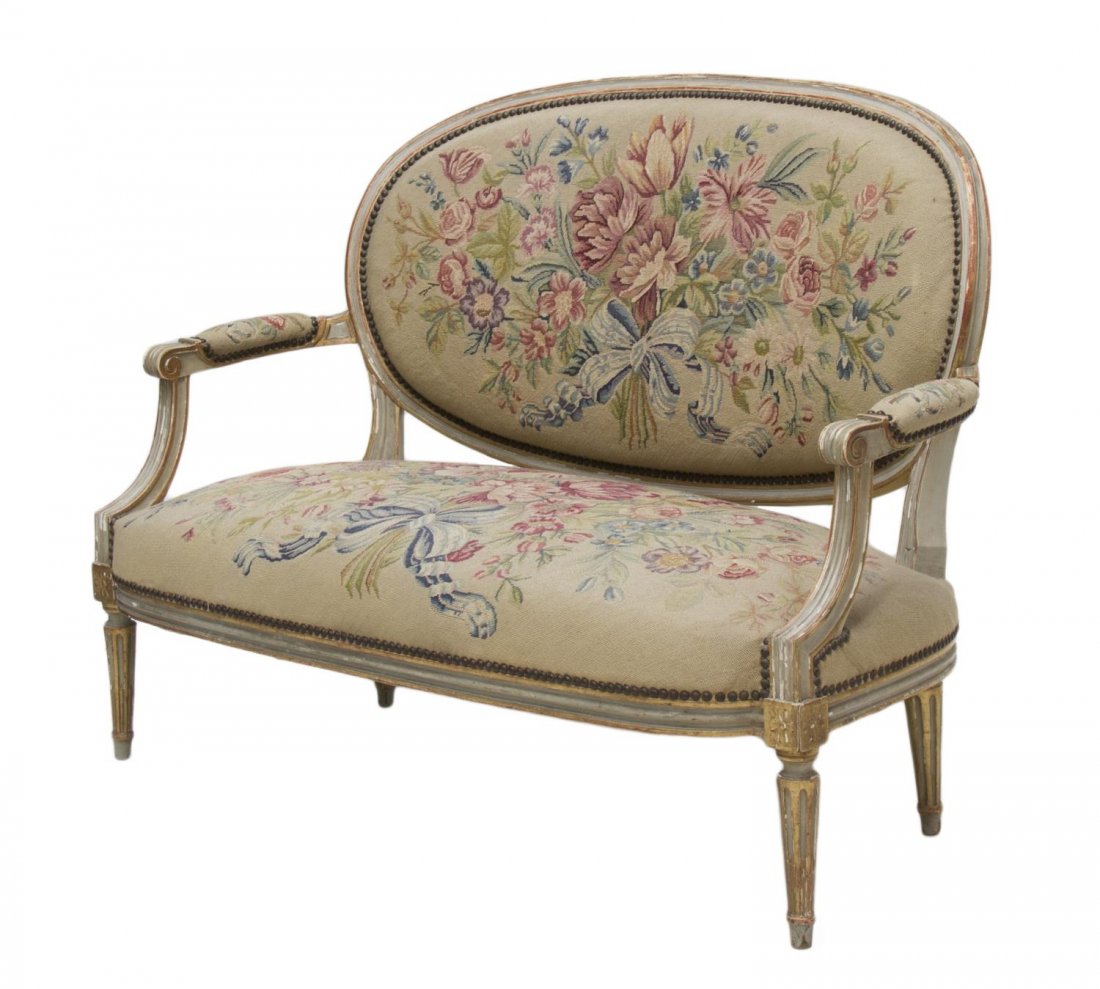 LOUIS XVI STYLE SETTEE: Louis XVI style settee, early 20th c., having a worn gilt and beige painted frame surrounding the oval back, shaped padded arms ending in scrolled handholds, the back and seat upholstered in floral an