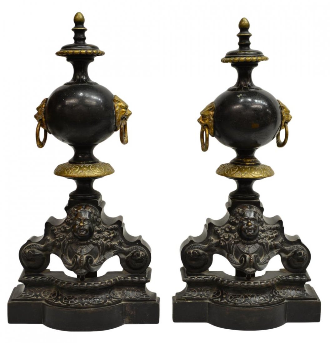 (2) VICTORIAN PARCEL GILT BLACK FIGURAL ANDIRONS: (pair) Victorian black metal and gilt andirons, the shaped base of each, surmounted by the robust face of a putti, lion masque ring handles further up the bulbous standard, concluding in a gilt finial