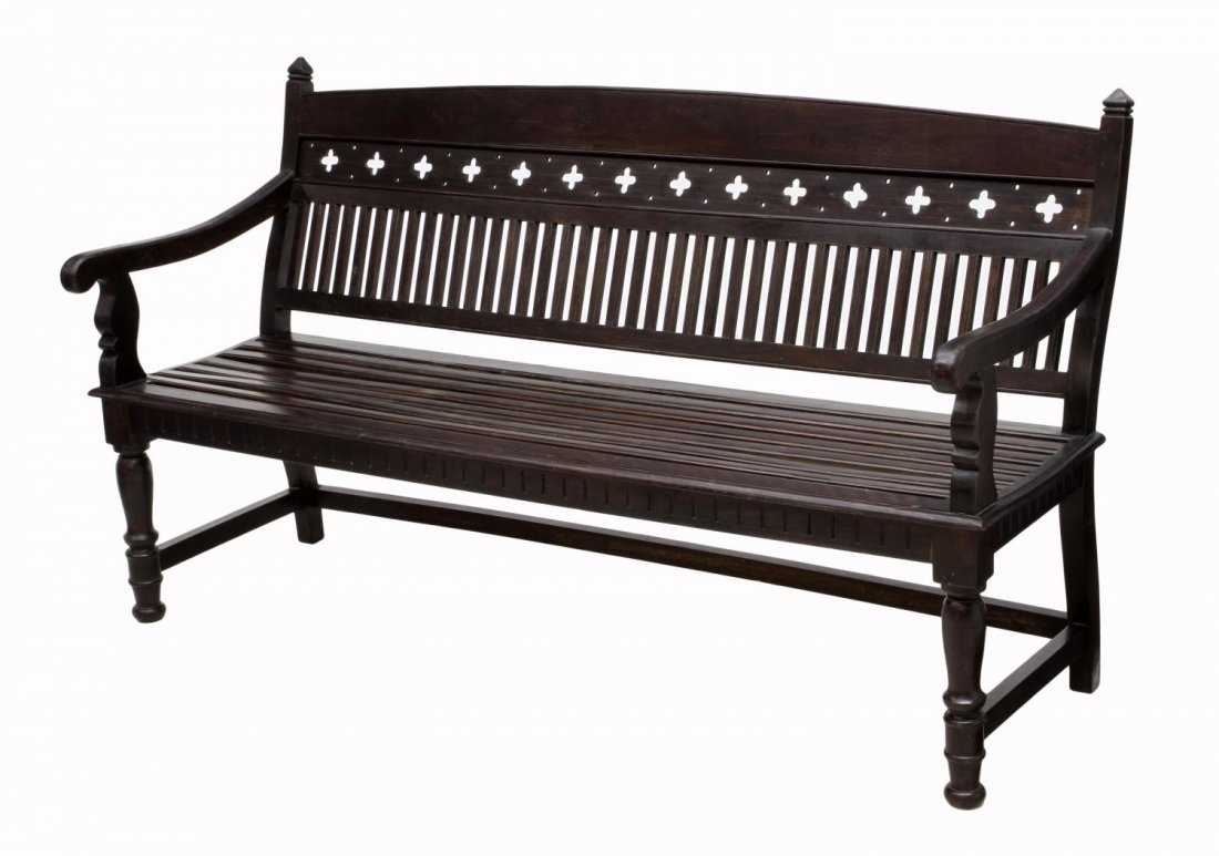 LONG TEAKWOOD QUATREFOIL BENCH: Long teakwood bench from a Catholic monastery, India, a bowed crest rail over quatrefoil carving with vertical rails, the slat seat flanked by shaped arms with scrolled hand holds, rising on stretcher