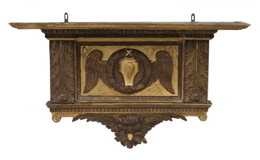 CONTINENTAL PARCEL GILT ARMORIAL CARVED WALL SHELF: Continental architectural parcel gilt carved wall hanging, the overhang shelf above acanthus pilasters, central heraldic wings in relief join a wreath with central shield, all above a figural masque, 