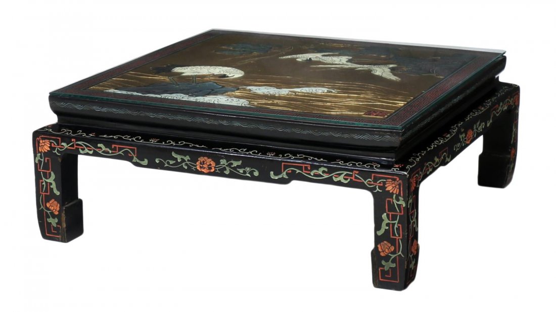 CHINESE BLACK LACQUER & GILT LOW TABLE: Chinese black lacquer low table, 20th c., the square top in a gilt finish with relief polychrome cranes in foliate, rising on short hoof feet, later glass top, 12.5"h, 32"w, 32"d Start Price: $150.00
