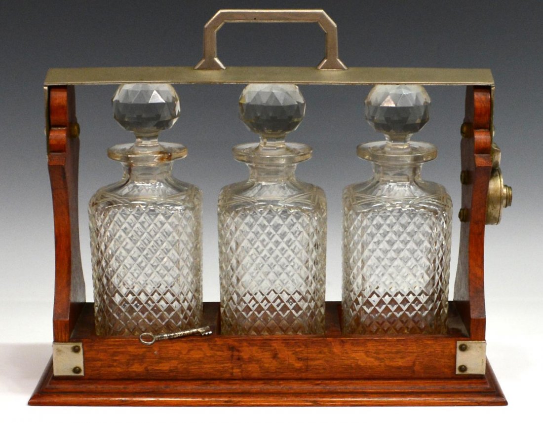 ANTIQUE OAK & METAL TANTALUS SET: Oak and metal tantalus set, lockable carrying handle, retaining key, enclosing three colorless cut glass decanters with faceted ball stoppers, each with diamond cut pattern, one with fracture to neck 