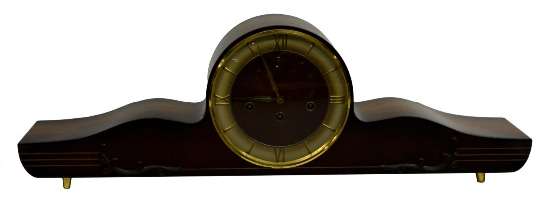 GERMAN HERMLE SCHWEBEANKER WESTMINSTER CLOCK: German Hermle Schwebeanker Westminster Art Deco style polished walnut mantle clock, a shaped case with circular wood face and gilt metal roman numerals behind a domed glass door, relief scroll work an