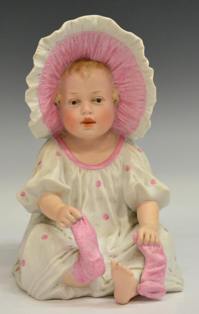 GERMAN GEBRUDER HEUBACH BISQUE PIANO BABY: German Gebruder Heubach bisque piano baby, wearing white and pink polka dot dress with bonnet and pink socks, incised sunburst mark and 3144 to the base, firing flaws as pictured, 9.5"h, 2.5lbs Start 