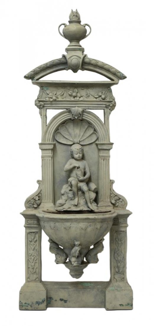 LARGE PATINATED BRONZE ARCHITECTURAL WALL FOUNTAIN: Patinated and painted verde bronze garden wall fountain, a flaming urn surmounting the architectural structure, centered by a robust figure in drapery, dolphins support the basin above an open pilaste