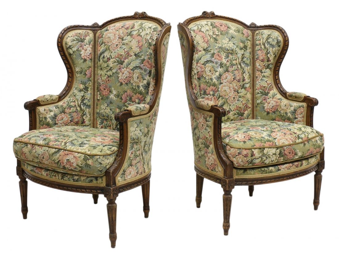 (PAIR) FRENCH LOUIS XVI STYLE BERGERES: French Louis XVI style bergeres, early 20th c., the natural wood frame with pierced floral crest, shaped wing sides, floral upholstery with removable seat cushion, rising on tapered ribbed legs with b
