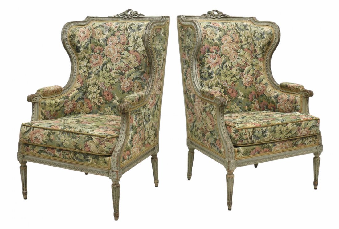 (PAIR) FRENCH LOUIS XVI STYLE BERGERES: French Louis XVI style bergeres, early 20th c., having a painted frame with pierced ribbon and floral crest, shaped wing sides, floral upholstery with removable seat cushion, rising on tapered ribbed 