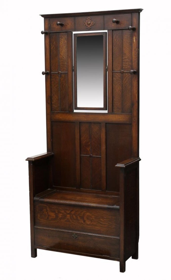 ENGLISH OAK HALL TREE: English oak bench seat hall tree, 1930's, a stepped cornice over a central tilting mirror, six coat hooks, the bench seat with lift top for storage, a lower drop front storage door, repair to hinged s