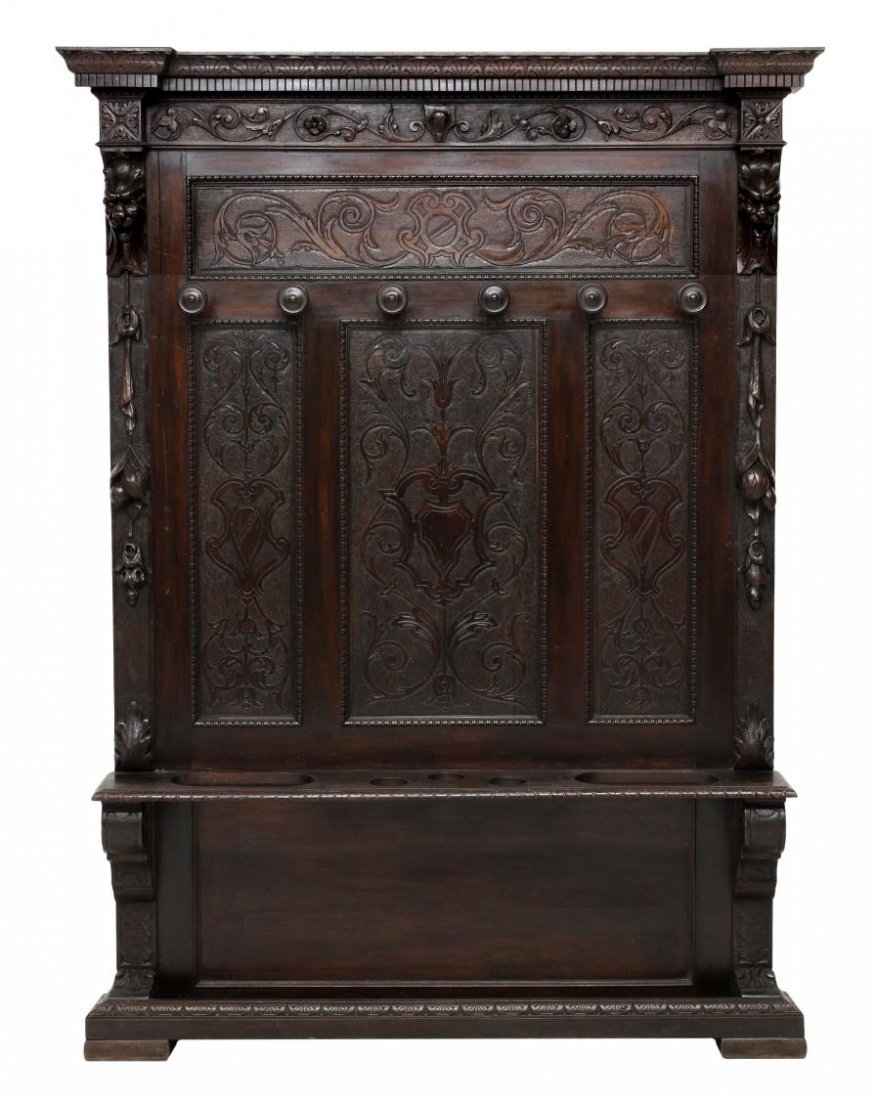 ITALIAN RENAISSANCE REVIVAL HALL TREE: Italian Renaissance Revival hall tree, c. 1900, a stepped cornice over foliate and relief carved decoration, two masks flanking the six coat hooks, a center shelf with umbrella rack, lacking lower dri