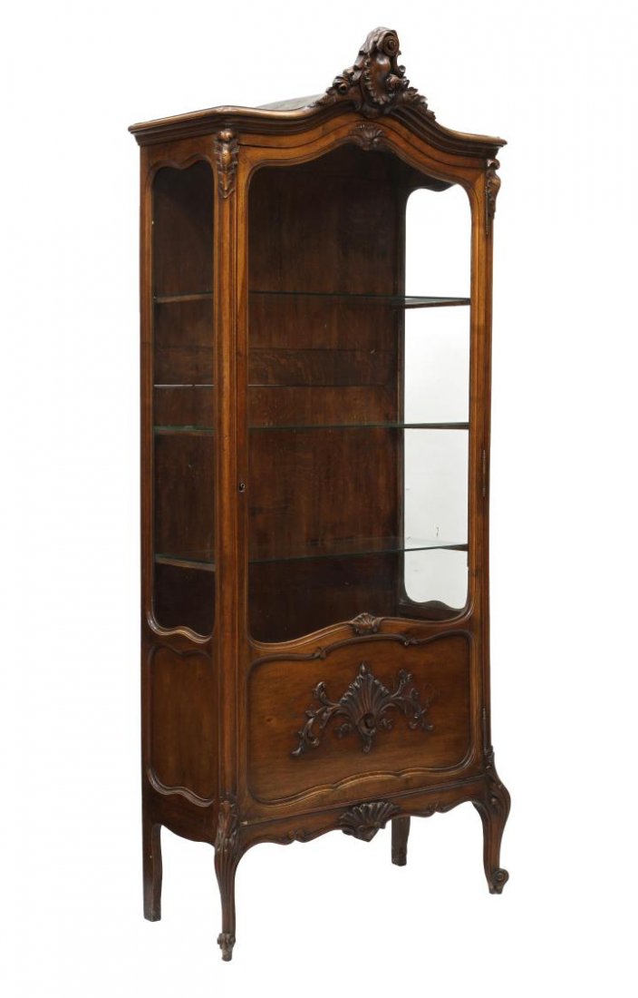 FRENCH LOUIS XV STYLE VITRINE: Louis XV style walnut vitrine, 20th c., ex. Hotel Aiglon, Menton, France, a shell crest at the shaped top over the parcel glazed door, the lower section with applied and incised foliate carving, inter