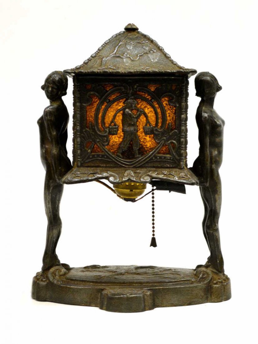 ART DECO DOUBLE NUDE ASIAN STYLE METAL TABLE LAMP: Art Deco metal table lamp, two female nudes hold the architectural center decorated in an Asian motif and lined with textured amber glass, hinged lid now loose, oval base centering a dragon, lacking f