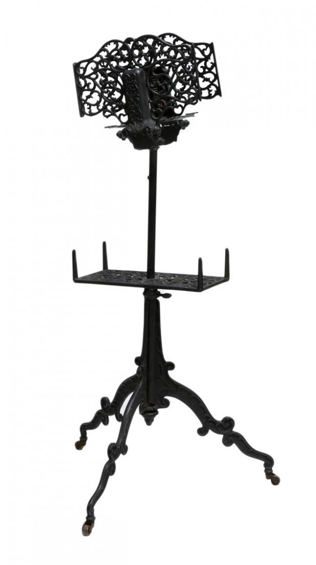 ANTIQUE AMERICAN WROUGHT IRON BOOKSTAND: American wrought iron adjustable bookstand, c. 1900, the upper part with a pierced spring opened book holder, rising on a central pedestal with lower shelf, a tripod base on castors, 38.5"h, 20"w, 20"
