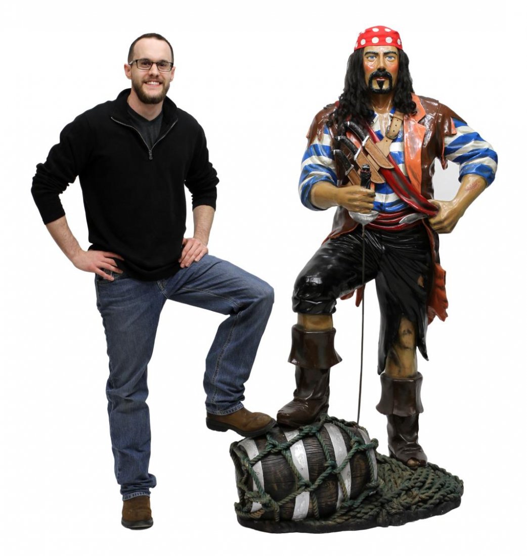 LIFE SIZE STATUE OF A PIRATE: Life size statue of a pirate, resin, a cloth bandana over his black hair, outfitted with faux knives, one hand rests on a faux sword while his foot rests on a rope and net covered barrel, approx. 72"h