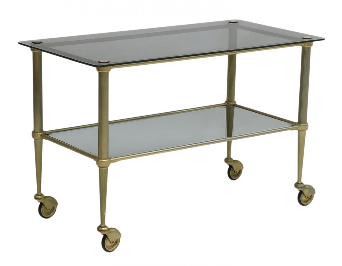 FRENCH BRASS & GLASS ROLLING SERVICE CART: French modern service trolley, c. 1970, in the manner of Maison Jensen, the brass frame holding two glass tiers, moving on wheels, approx 21.5"h, 33"l, 17"d Start Price: $150.00