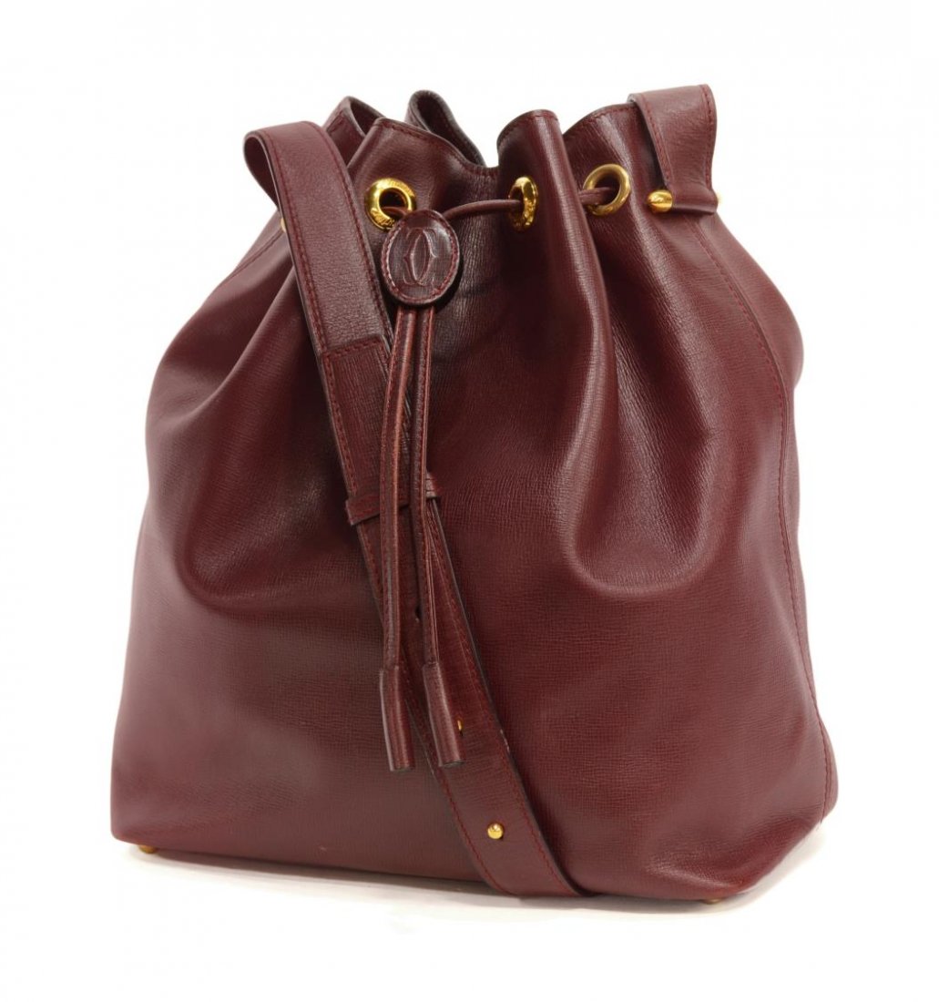 CARTIER BURGUNDY LEATHER DRAWSTRING BUCKET BAG: This retro-chic leather drawstring bucket bag with adjustable leather shoulder strap, Cartier logo oval on drawstring, front gold tone metal grommets marked Cartier, the rest plain,leather on interior