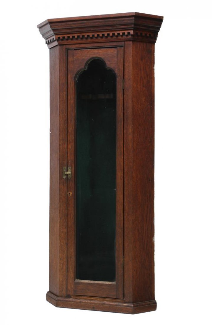 AMERICAN OAK GUN CORNER CABINET: American oak gun corner cabinet, 19th c., a stepped cornice with dentil moulded frieze over trefoil framed door opening to the felt lined interior with a two gun rack, 55.5"h, 26"w, 14"d *Provenance: 