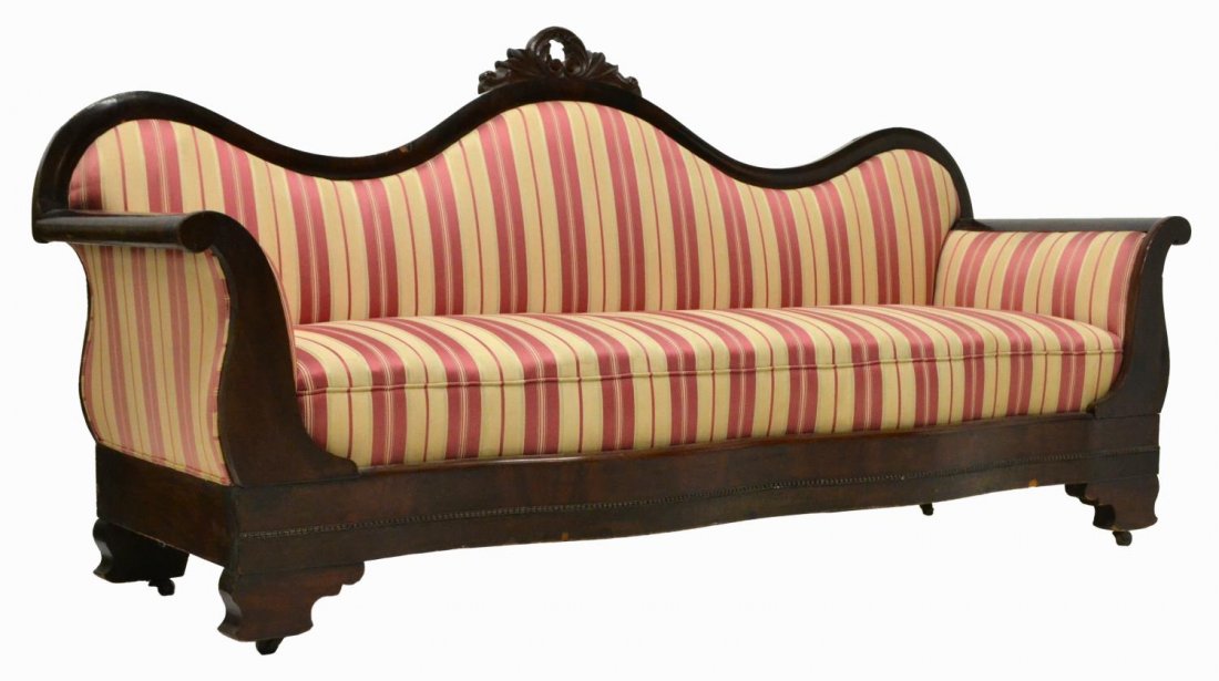 AMERICAN EMPIRE REVIVAL MAHOGANY CARVED SOFA: American Empire Revival sofa, 19th c., carved wood frame with central floral crest, outward scrolled arm rests, seat and back upholstered in striped fabric, shaped skirt over four legs, worn fabric, m