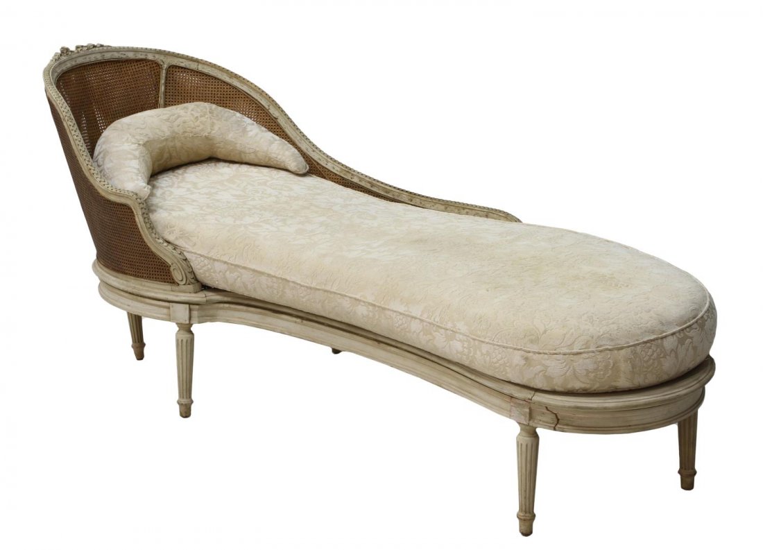LOUIS XVI STYLE PAINTED CHAISE LOUNGE: Louis XVI style Recamier, 19th c., carved top rail with floral crest, caned back and seat holding white fabric upholstered seat cushions, fluted legs, some losses, approx 35"h, 60.5l, 29.5"w *Provenan