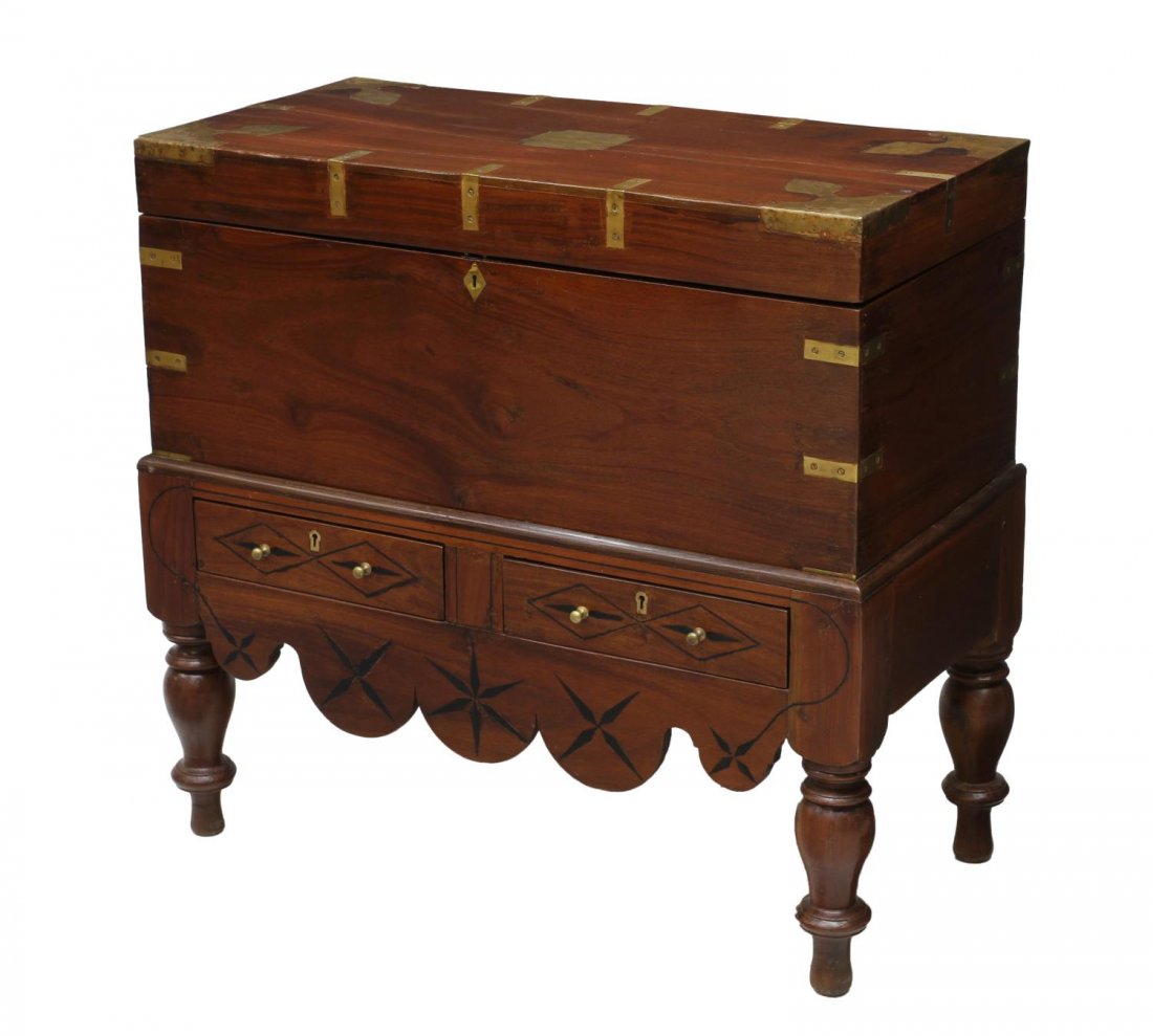 BRITISH COLONIAL BRASS BOUND CHEST ON STAND: British Colonial mahogany trunk on stand, c.1900, brass bound with foliate shape brass at lift top, lower stand with two drawers, dark wood accents, rising on turned legs with arrow feet, wood splitti